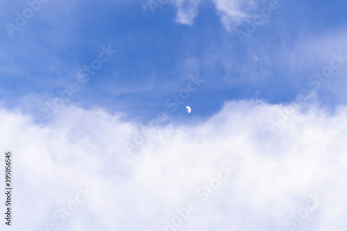 Blue bright sky with white clouds. Moon in daylight