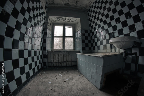 Old and terrible ruined bathroom in an old abandoned manor house. Checkered tiles on the walls. Gloomy atmosphere.