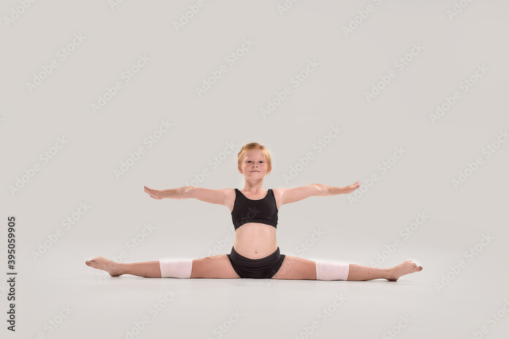 Full length shot of cute little redhead girl child looking at camera, doing splits, showing flexibility isolated over grey background Full length shot of cute little redhead girl child looking at camera, doing splits, showing flexibility isolated over grey background