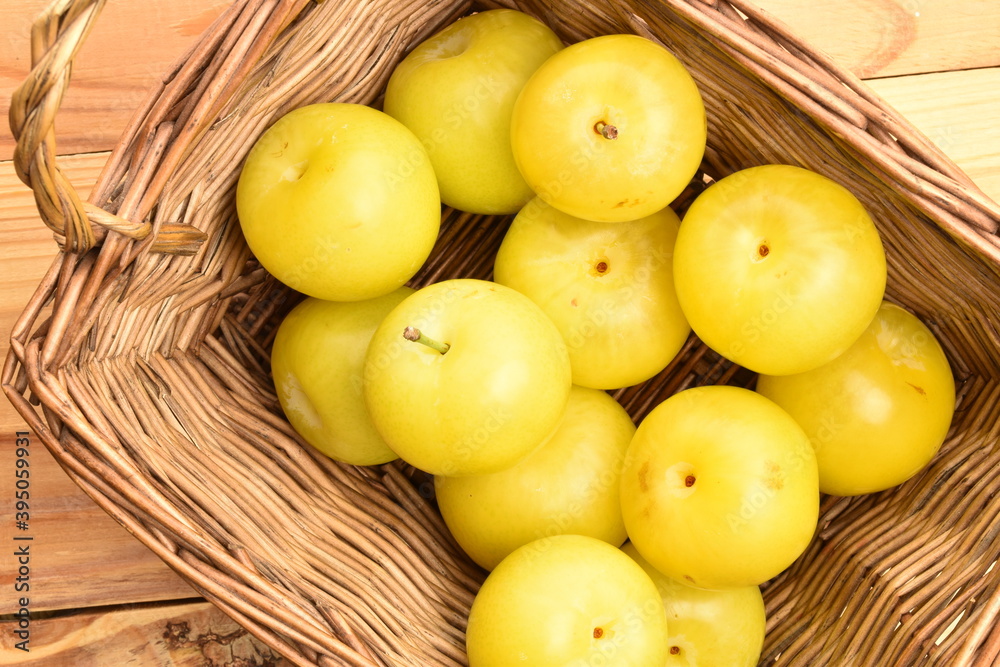 Several bright yellow plums, close-up, on a white wooden table.