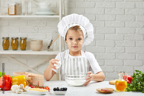 little boy in chef hat and an apron cooking dough for pizza in the kitchen. child cooking with eggs