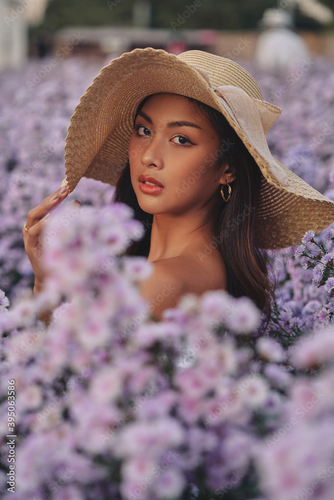 closeup fashion portrait of stylish young asian woman with straw hat posing at the flowers field