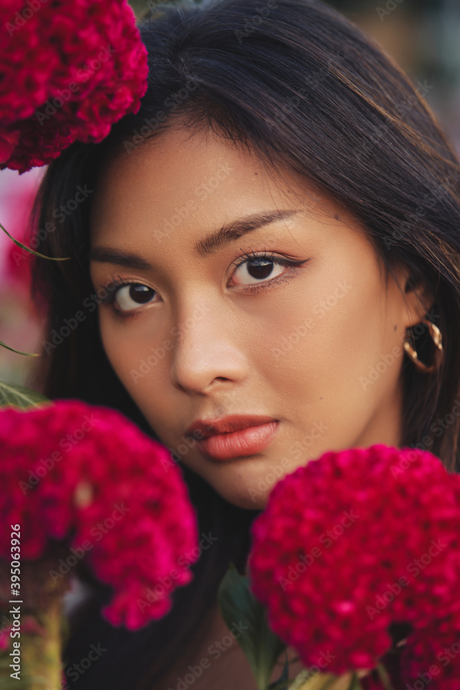 closeup portrait of a beautiful young Thai woman surrounded by red flowers. Spring blossom