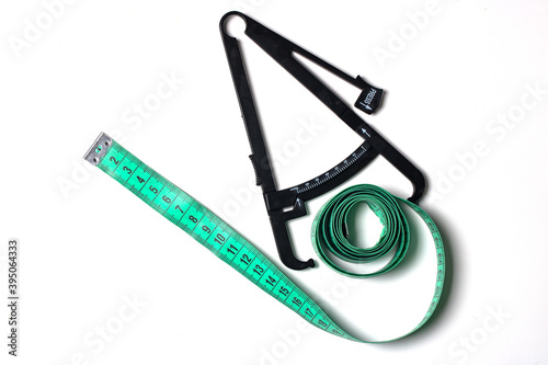 Personal accurate body fat tester. Concept of body weight control. Skinfold belly caliper and measuring green tape on white background.