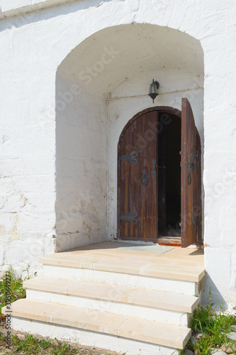 An old wooden door in the white fortress wall © alexnikit