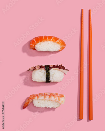 Sushis or nigiris with orange chopsticks over a pink background