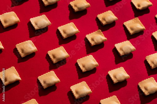 Pattern of raw ravioli over a red background with hard and dark shadows
