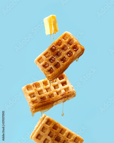 Flying waffles and butter getting dripped with maple syrup over a light blue background photo