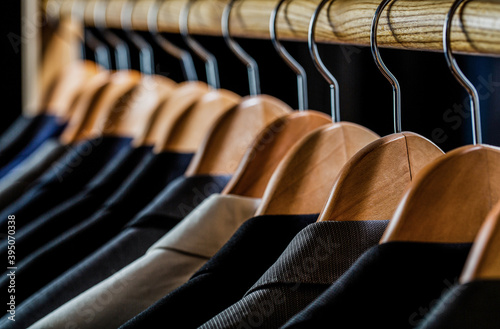 Mens suits in different colors hanging on hanger in a retail clothes store, close-up. Mens shirts, suit hanging on rack