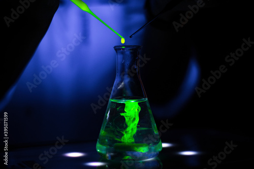  European researcher working with a green fluorescent compound in dark chemistry laboratory for pharmaceutical
