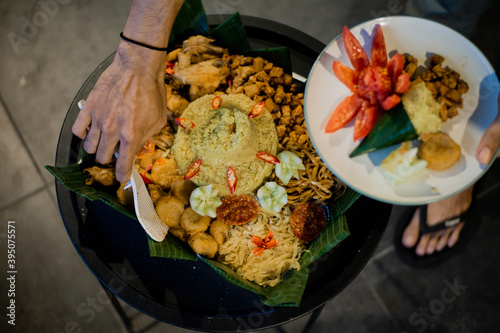 View of people hands taking Nasi Tumpeng dish, Indonesia authentic culinary,made from steamed rice yellow and some dishes,usually serving for special occasion such as birthday party 