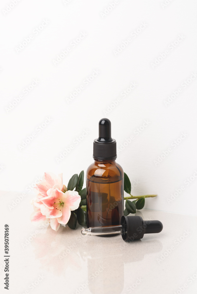 A glass dropper bottle with a pippette with black rubber tip and beautiful flower on grey background. Nature Skin concept. Organic Spa Cosmetics. Close up.
