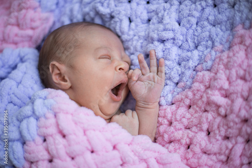 Newborn baby yawns and lies on a pink blanket