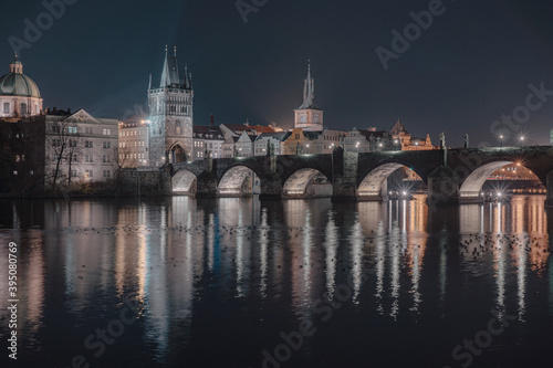  illuminated Charles Bridge from 14 centuries and light from street lighting and stone sculptures on the bridge and light reflections on the surface of the Vltava river at night in Prague