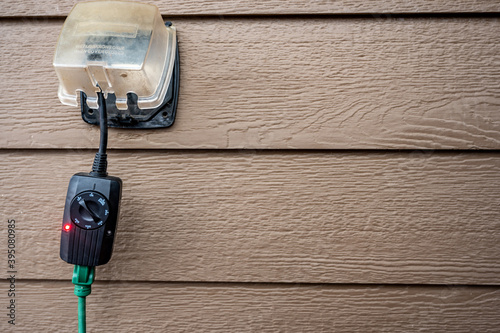 Outdoor timer and GCFI outlet with cover.  Brown siding on residential building photo