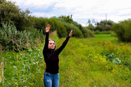 beautiful brunette girl in purple golf near a green bush with a flower in her hair raised her hands up to the sky