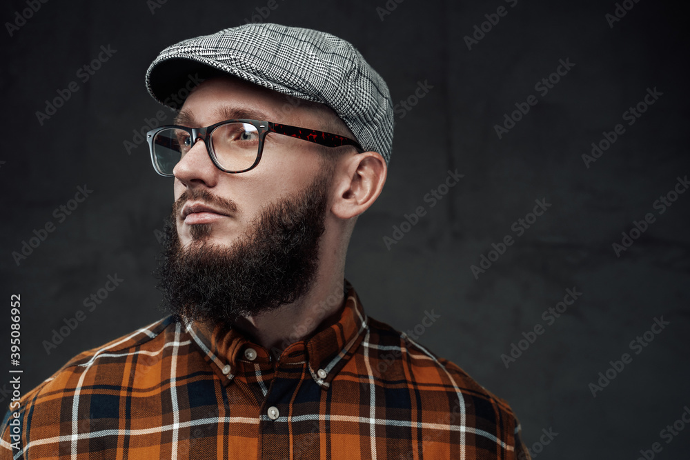 Portrait of stylish and brutal guy with glasses and beard weared with cap he looks away in dark background. Portrait of stylish and brutal guy with glasses and beard weared with cap he looks away in dark background.