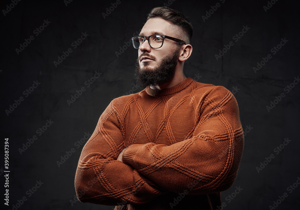 Posing in dark background with crossed arms strong guy in sweater with glasses and beard.