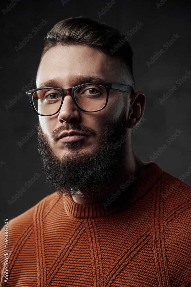 Obraz premium Bearded manly hipster with stylish hairstyle and beard posing in dark background weared with glasses.