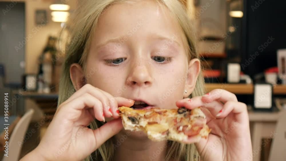 Portrait of a 9 years old blonde girl biting pizza slice in restaurant. Close-up shot. Portrait of a 9 years old blonde girl biting pizza slice in restaurant. Close-up shot.