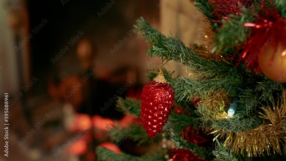 Woman puts a beautiful red decoration on a branch of a christmas tree, with a fireplace in the background. She wears a white wool sweater. Beautiful christmas scene Woman puts a beautiful red decoration on a branch of a christmas tree, with a fireplace in the background. She wears a white wool sweater. Beautiful christmas scene