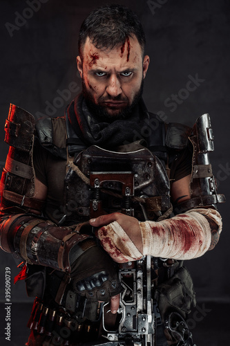 Portrait of staring at camera with serious face stalker with damaged and bandaged arm holds his shotgun in dark background.