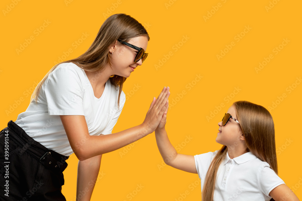 Family team. Positive lifestyle. Understanding support. Happy mother and little daughter girl in sunglasses giving high five isolated on orange empty space background.