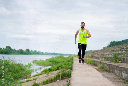 Athletic jogging asian man in stylish sportswear on workout outside in cloudy weather on embankment