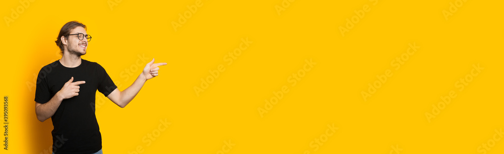 Handsome caucasian man with beard and eyeglasses pointing to the free space on a yellow wall Handsome caucasian man with beard and eyeglasses pointing to the free space on a yellow wall