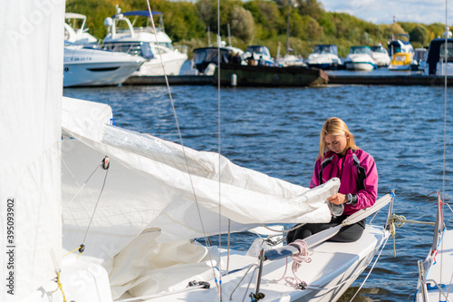 At the yacht parking lot, a young yachtsman in a pink windbreaker prepares her boat for a sailing competition