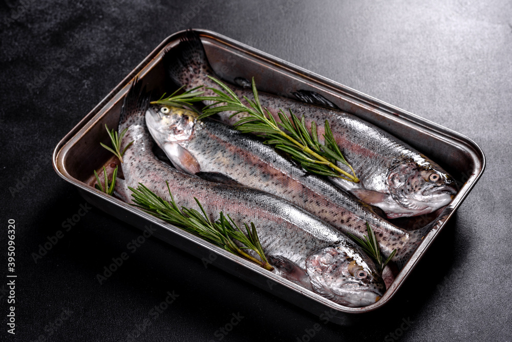 Raw trout lie on a black stone chopping board on a dark concrete table
