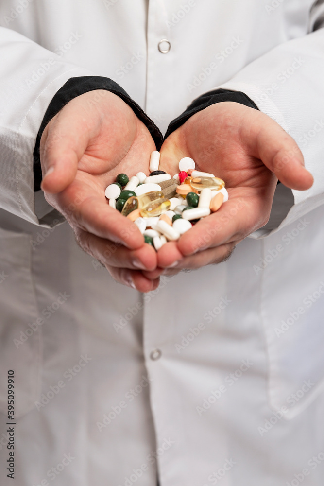 A doctor in a dressing gown holds a handful of multicolored pills and capsules in his hands. Pharmacology and Medicine. Vertical. A doctor in a dressing gown holds a handful of multicolored pills and capsules in his hands. Pharmacology and Medicine. Vertical.