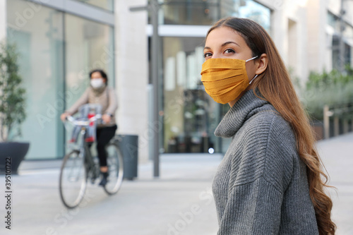 Confident young woman with protective mask looks around sitting on bench waiting for better times in modern city