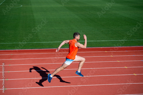 athletic muscular man running on racetrack at outdoor stadium, finish