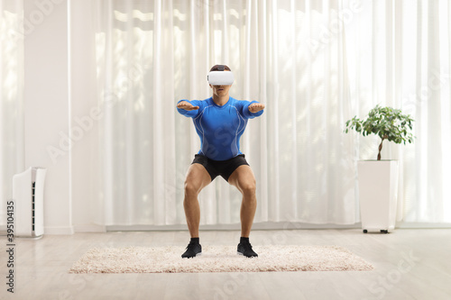 Muscular man exercising squats with a VR headset
