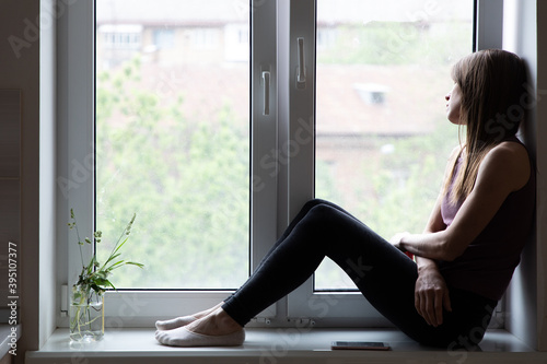 Tired young woman sitting on window sill and relaxing