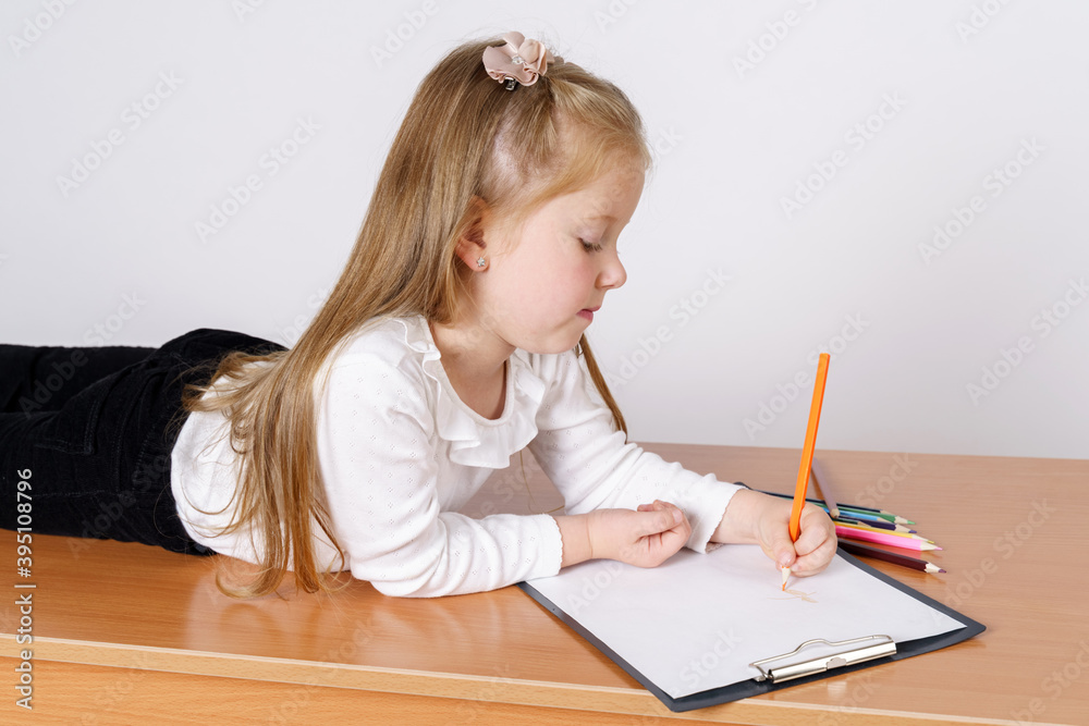 The girl lies and draws on a sheet of paper with pencils. Isolated over white background. The girl lies and draws on a sheet of paper with pencils. Isolated over white background.