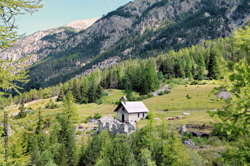 Petite chapelle entourée de chevaux dans une vallée des Alpes françaises.