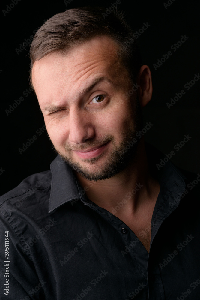 Studio portrait of a young caucasian man in a black blazer, looking at the camera, standing against plain studio background