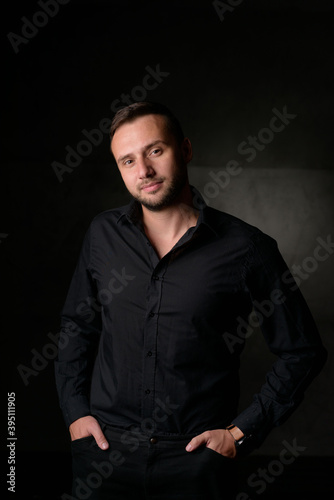 Studio portrait of a young caucasian man in a black blazer, looking at the camera, standing against plain studio background