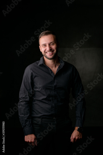 Studio portrait of a young caucasian man in a black blazer, looking at the camera, standing against plain studio background