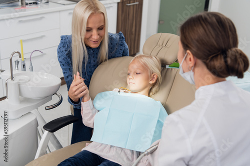 A parent and a scared child at the dentist's office, the mother is holding her daughter's hand, trying to comfort her.
