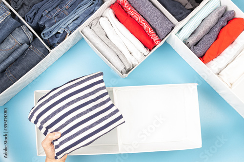 Female hands folding and puting clothes to baskets. Vertical storage of clothing, tidying up, room cleaning. Marie Kondo style of garments declutter and sorting. Top view photo