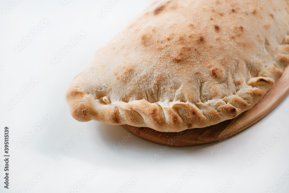 Italian pizza calzone on a wooden board. Italian pie in closed form of pizza made in the shape of a crescent. Italian fast food delivery. Side view.