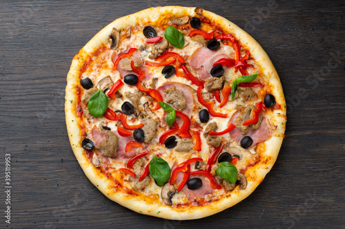 Italian pizza with melted mozzarella cheese, olives and sausage garnished with fresh vegetables and basil leaves