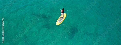 Aerial drone ultra wide top down photo of fit unidentified woman paddling on a SUP board or Stand Up Paddle in Mediterranean turquoise clear sea
