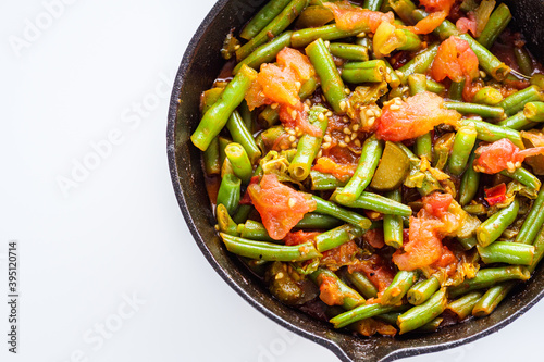stewed green beans in a cast iron skillet on a white background