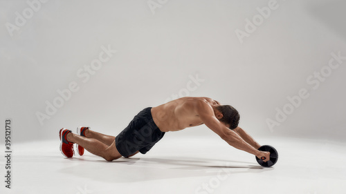 Fototapeta Naklejka Na Ścianę i Meble -  Muscular sportsman exercising with fitness ab roller