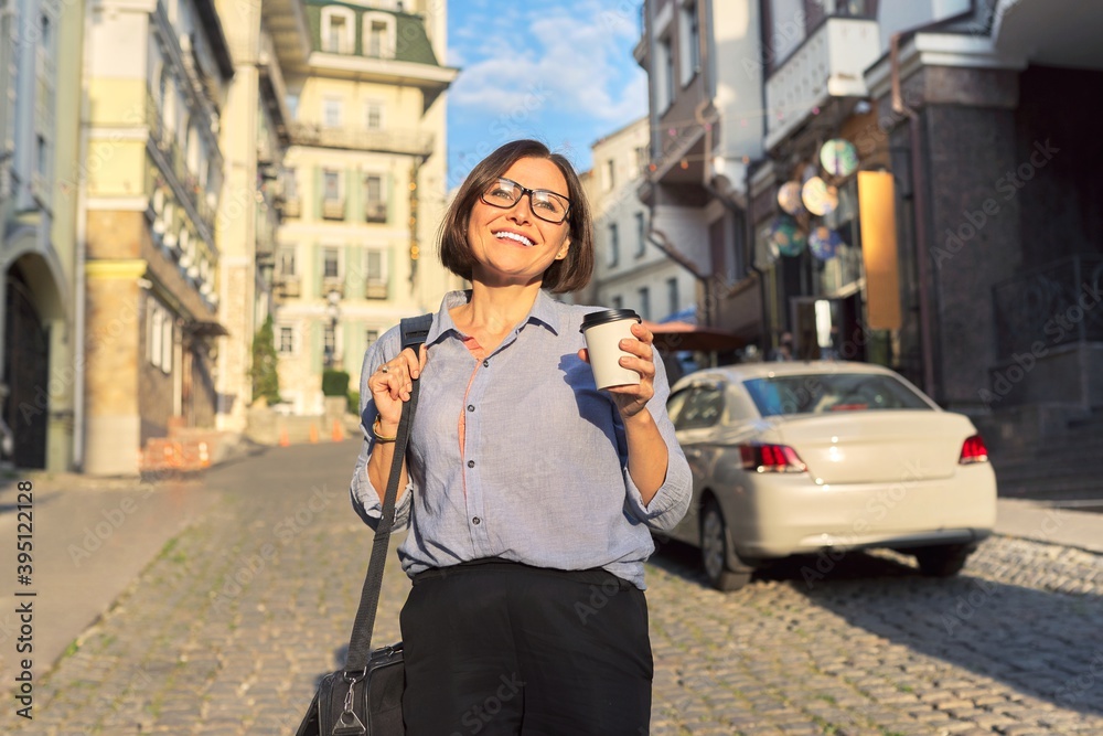 Mature business woman in glasses with office laptop bag walking along city street Mature business woman in glasses with office laptop bag walking along city street