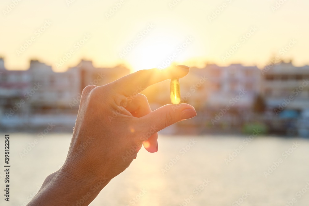 Obraz na płótnie Yellow gel capsule vitamin d omega-3 in womans hand, sun sea background w salonie